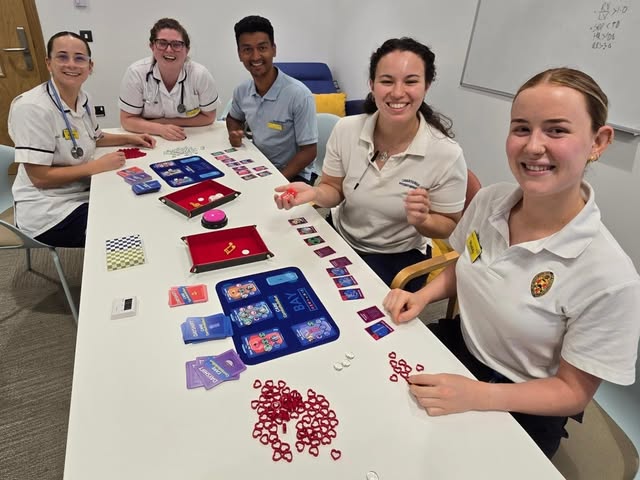 A group in healthcare uniforms playing Dayshift around a table